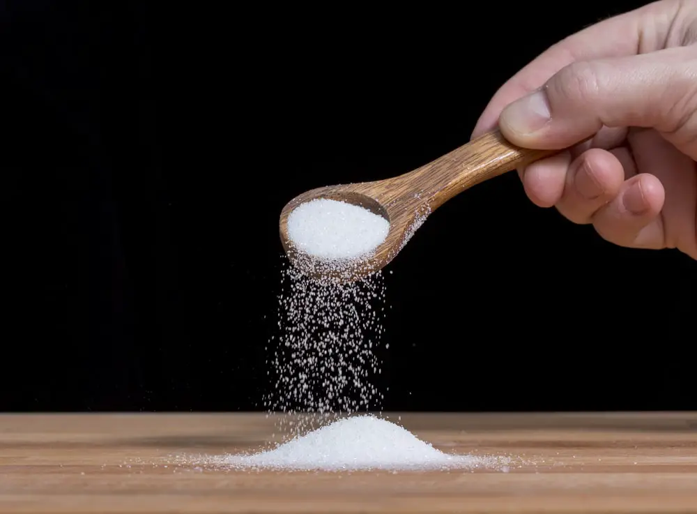 person-pouring-sugar-salt-wooden-spoon
