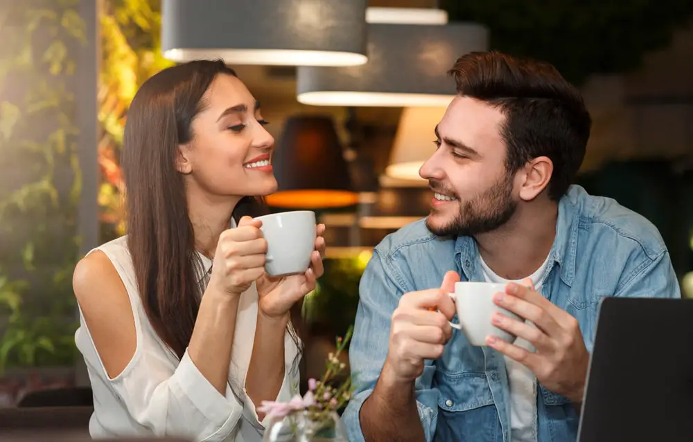 Young couple tasting coffee drinks enjoying flirt and conversation during weekend date sitting in cozy cafe