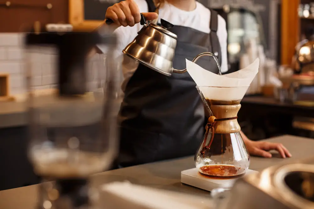 Professional barista preparing coffee using chemex pour over coffee maker and drip kettle